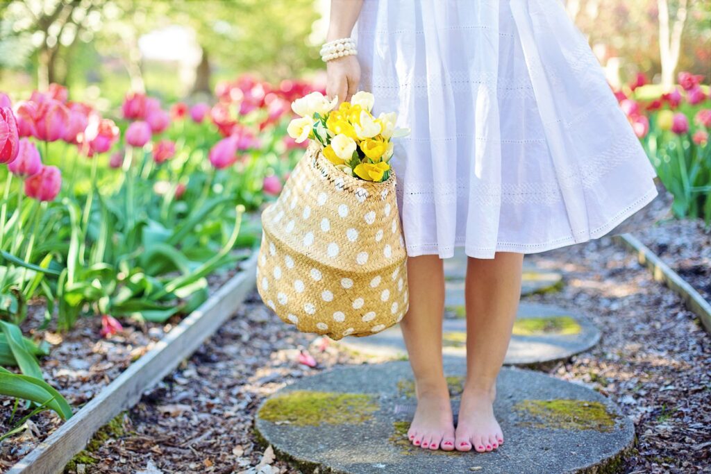 Bilden visar en person med bara fötter och plockade blommor i en korg. Plantera blomsterlökar enkelt och njut av vackra blommor i din egna trädgård.
